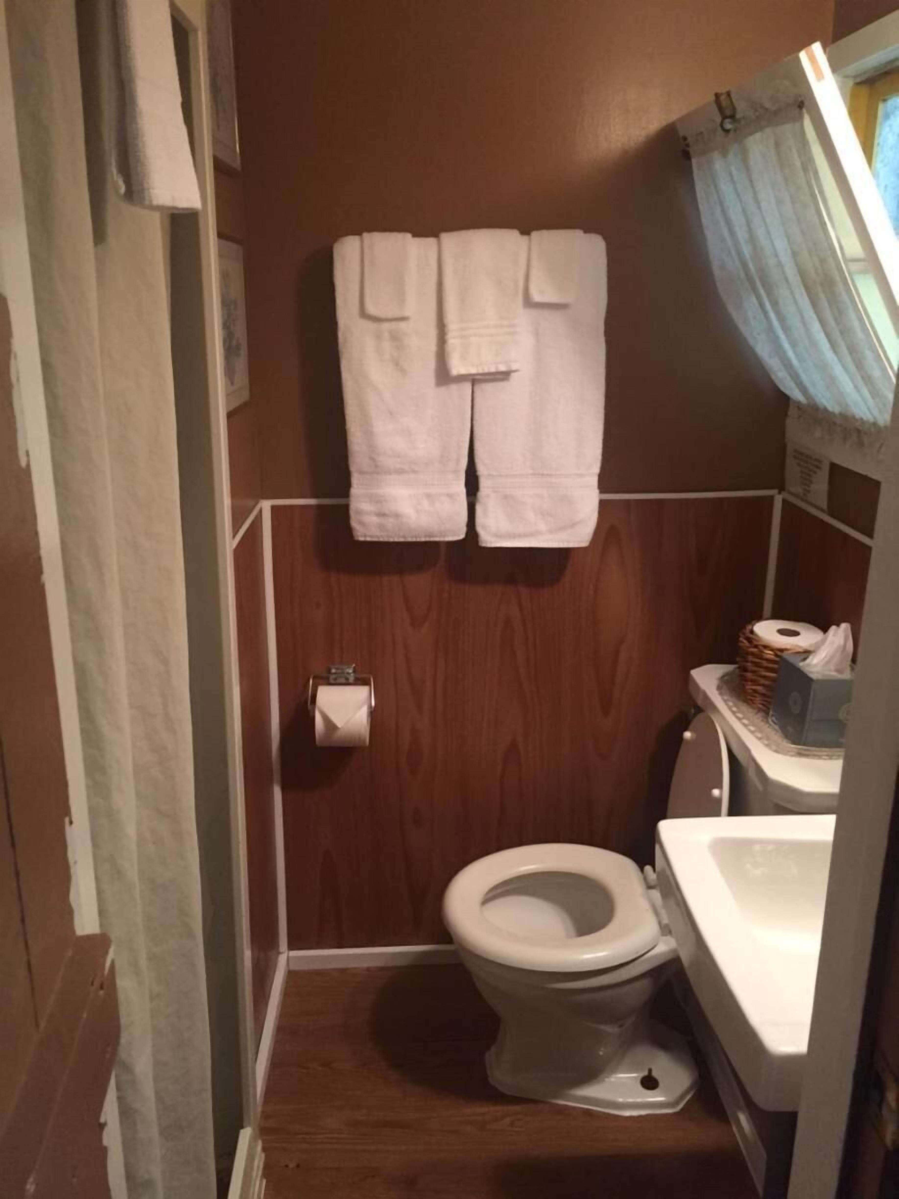 A compact bathroom with a wooden floor, a toilet, a sink, and a towel rack with two towels.