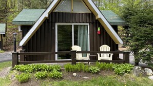 A cabin with a triangular roof, a front porch with chairs, and a fire extinguisher mounted on the wall. - Amber Lantern Lake George Motel and Cottage Rentals (Lake George)