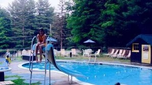 A swimming pool with a slide, surrounded by lounge chairs and a small building. - Amber Lantern Lake George Motel and Cottage Rentals (Lake George)