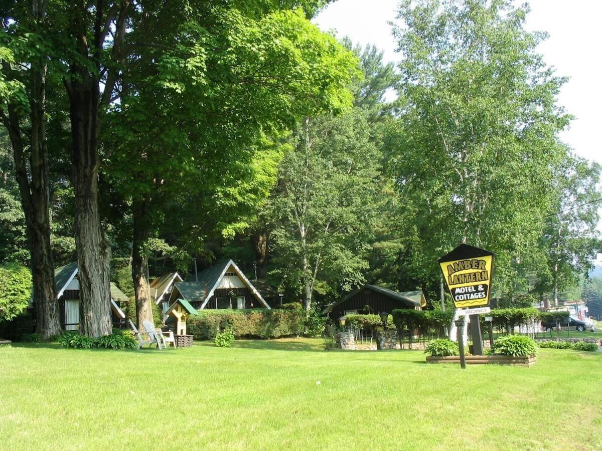 A sign for Amber Lantern Motel & Cottages with a grassy area and several wooden cabins.