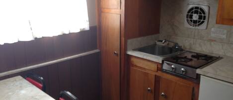 A compact kitchen with wooden cabinets, a gas stove, a sink, and a window with curtains.