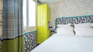A room with a bed, a yellow door, patterned wallpaper, and a window.