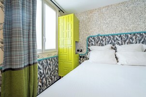 A room with a bed, a yellow door, patterned wallpaper, and a window.