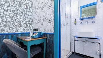 A bathroom with a tiled wall, a sink, a mirror, and a shower area.