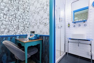 A bathroom with a tiled wall, a sink, a mirror, and a shower area.
