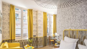 A hotel room with a bed, a yellow armchair, a small table with a lamp, and a window with yellow curtains. - Hôtel Crayon Rouge (Paris)