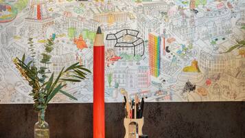 A desk with a vase of green plants, a tall red pencil, and a pencil holder with various writing instruments.