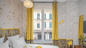 A hotel room with a bed, a desk, a chair, a telephone, and a window with yellow curtains. - Hôtel Crayon Rouge (Paris)