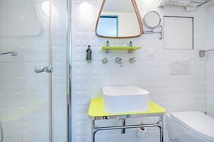 A modern bathroom with a glass shower enclosure, a white sink with a yellow countertop, and a mirror above the sink.