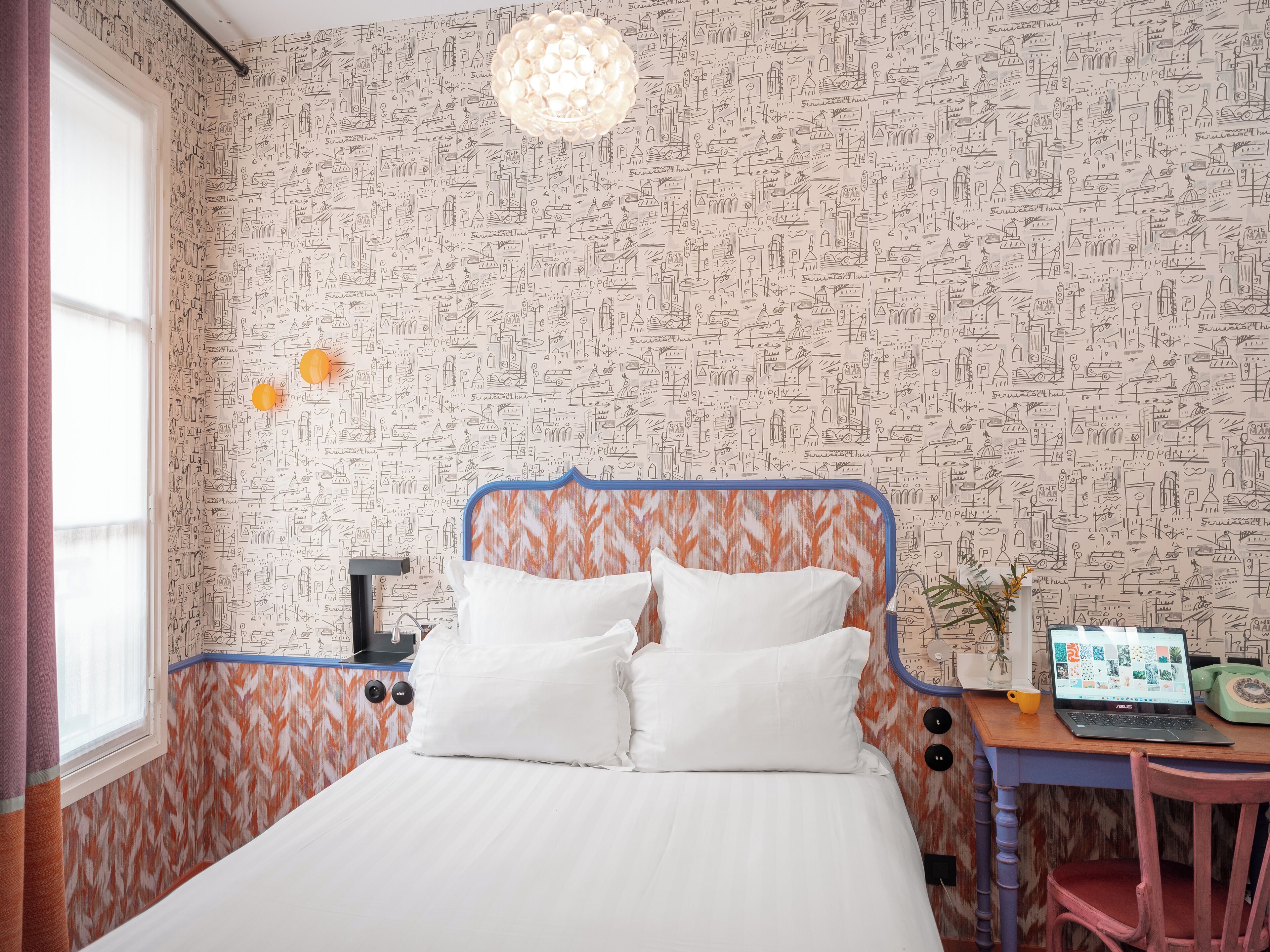 A bedroom with a bed, a desk with a laptop, and a vintage telephone.