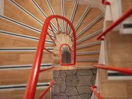Eine Wendeltreppe mit roter Handlauf und einem geometrisch gemusterten Boden.