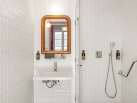 A bathroom with a white sink, a mirror with a wooden frame, a glass shower enclosure, and toiletries on the wall.