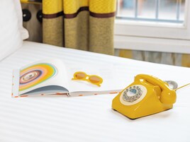 A bed with a book, yellow sunglasses, and a yellow rotary phone.