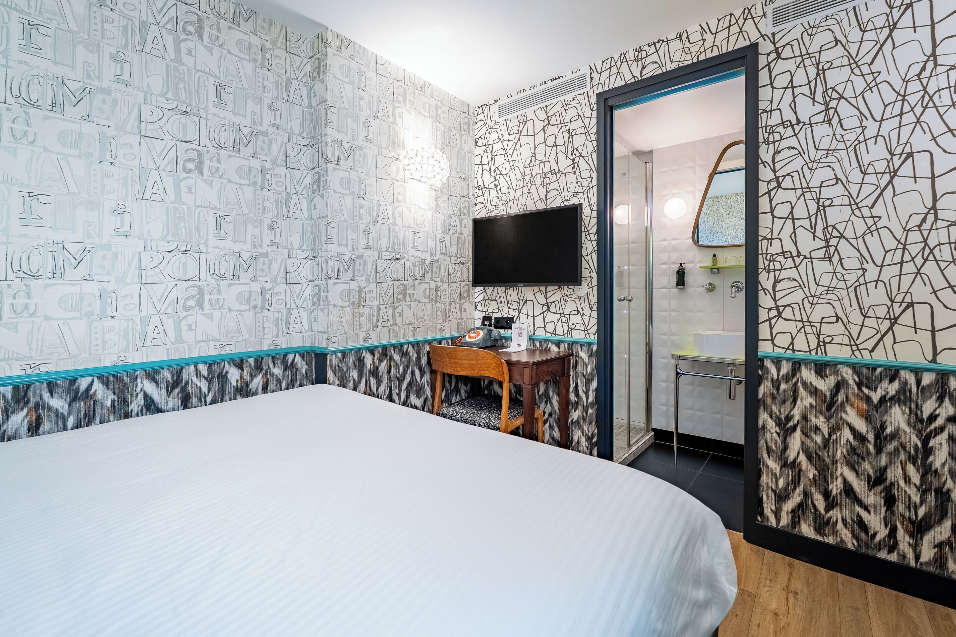 A hotel room with a bed, a desk with a chair, a flat-screen TV, and a bathroom visible through an open door.