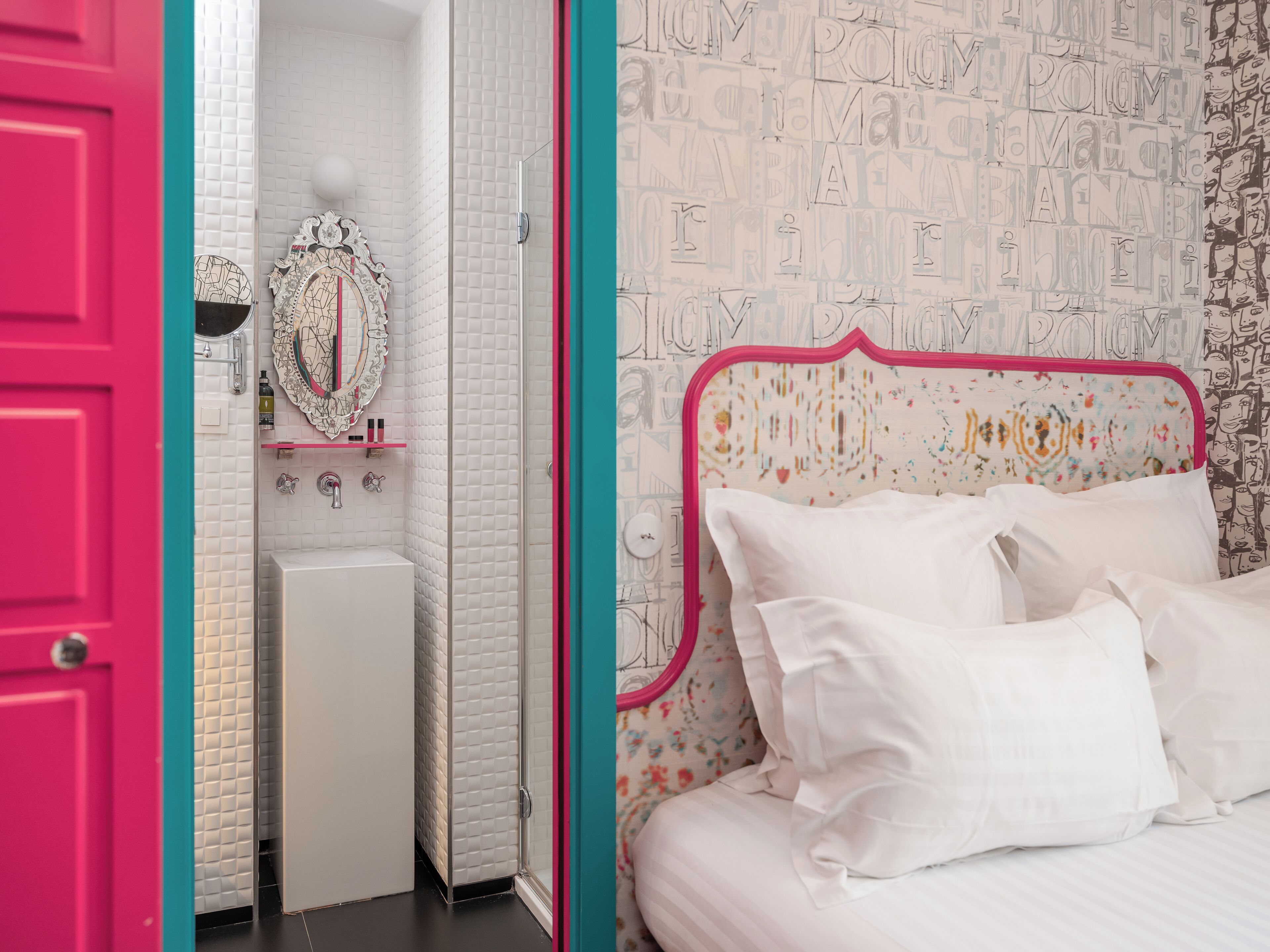A bedroom with a bed, a nightstand, and a mirror. There is a bathroom with a sink and a toilet. The room has a white tiled wall and a pink door.