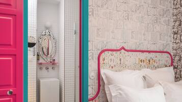 Un dormitorio con cama, mesita de noche y espejo. Incluye un baño con lavamanos y retrete. La habitación tiene una pared de azulejos blancos y una puerta rosa.