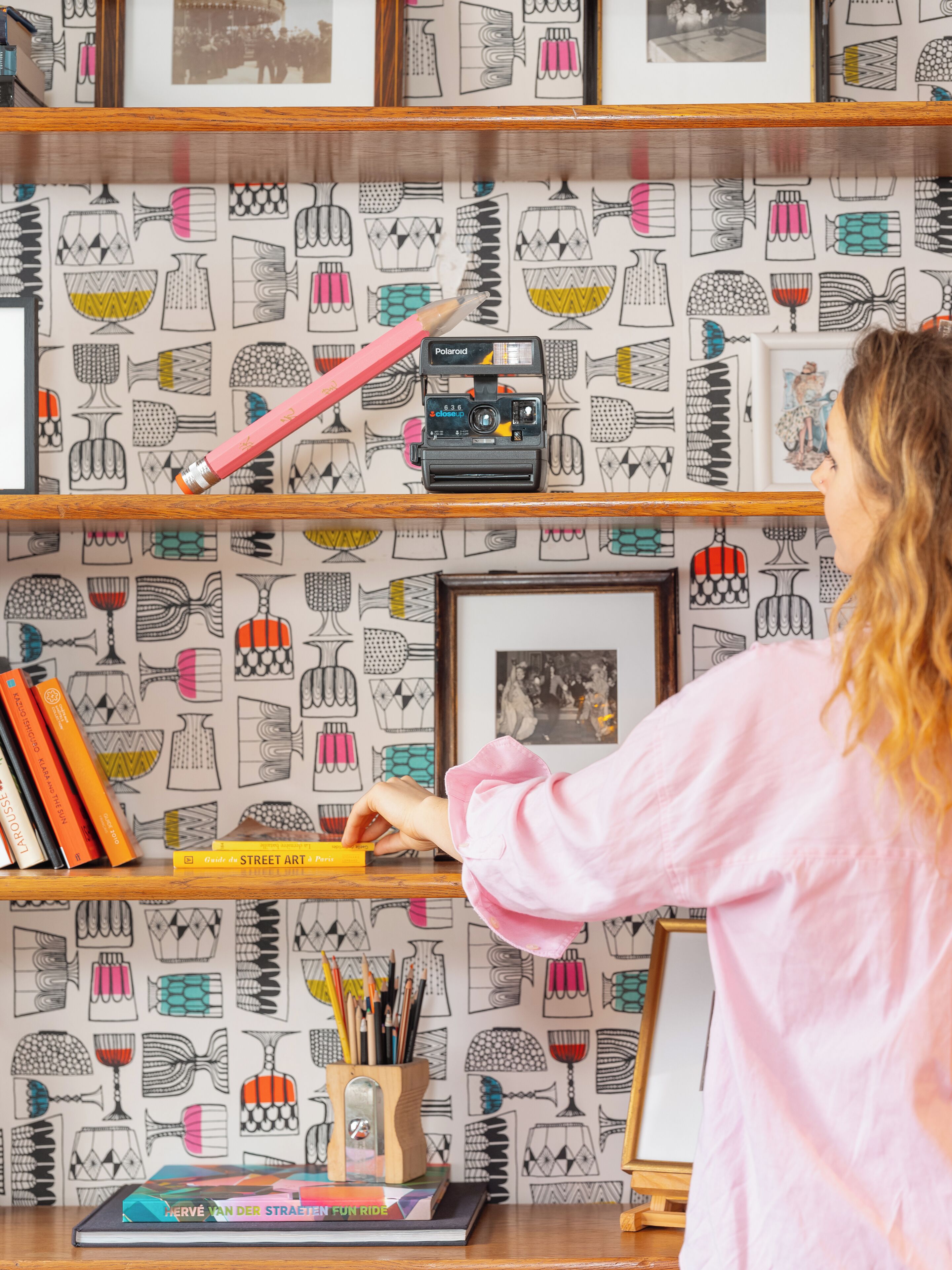 Una persona ordenando libros en un estante con un fondo de papel tapiz estampado.