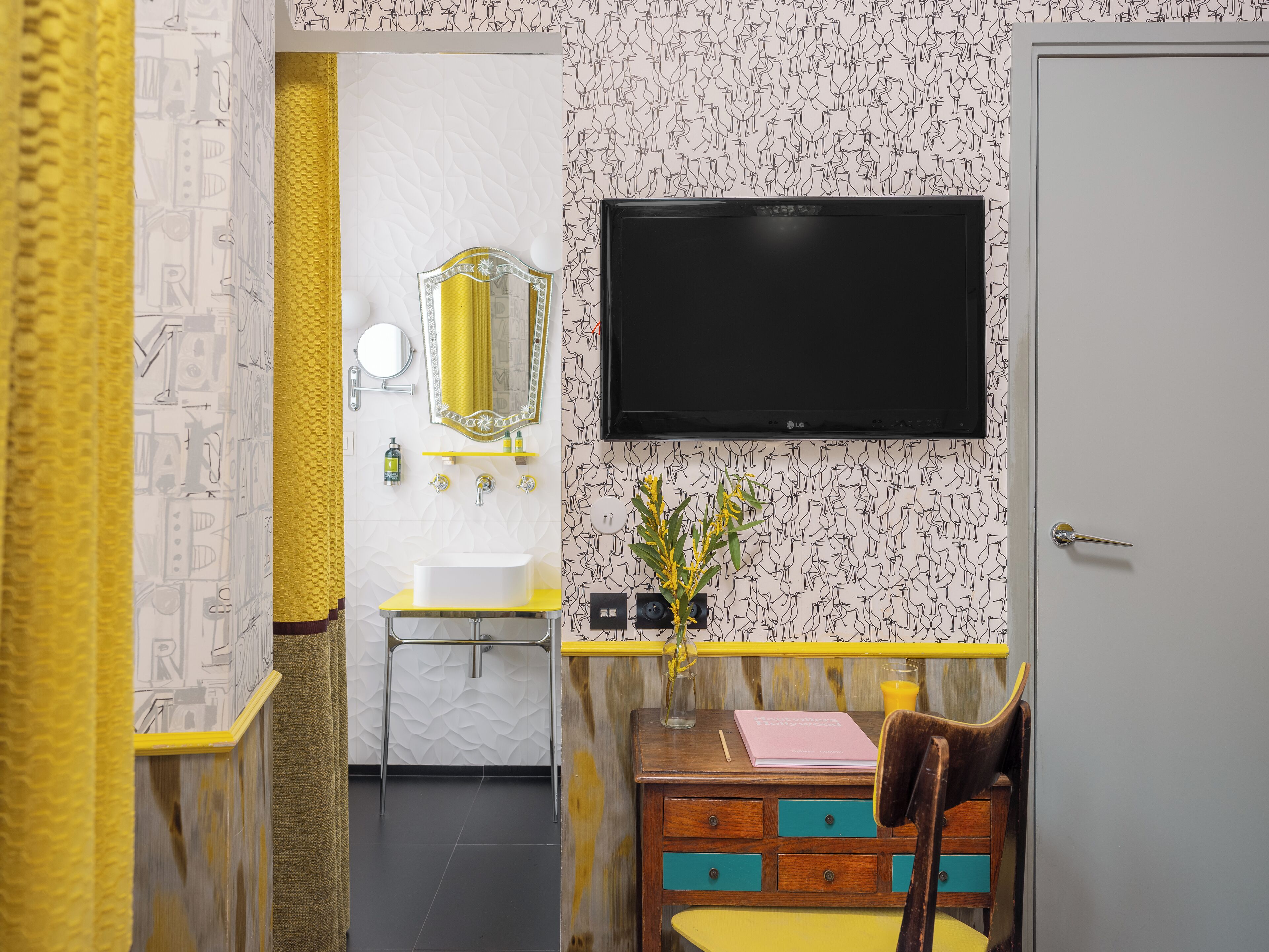 A bathroom with a sink, mirror, toilet, and a television mounted on the wall.
