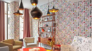 A modern living room with a sofa, armchairs, a coffee table, and a bookshelf. - Hôtel Crayon Rouge (Paris)