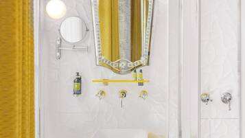 Un baño con un lavamanos blanco, un espejo con luces y un perchero amarillo.