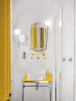 A bathroom with a white sink, a mirror with lights, and a yellow towel rack.