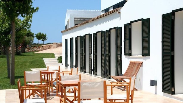 Un patio al aire libre con muebles de madera y vistas a un edificio blanco con persianas.