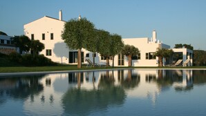 Un edificio moderno blanco con una piscina que refleja árboles y un cielo despejado.