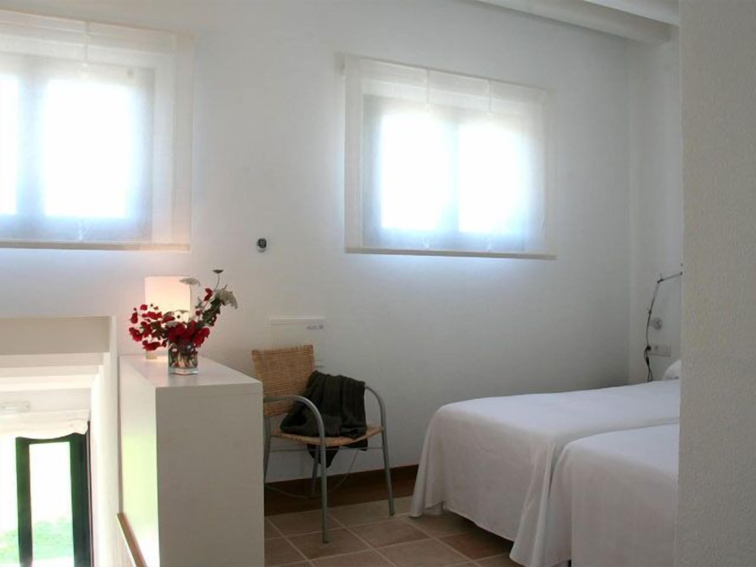A room with two beds, a chair, a table, and a window with curtains.