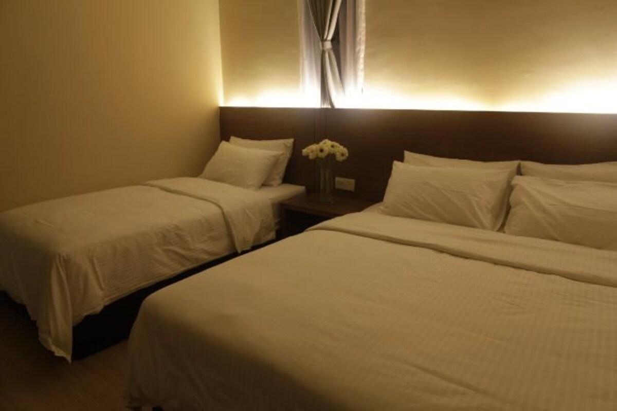 Habitación de hotel con dos camas individuales, una mesita de noche con un florero y un cabecero con cortinas.