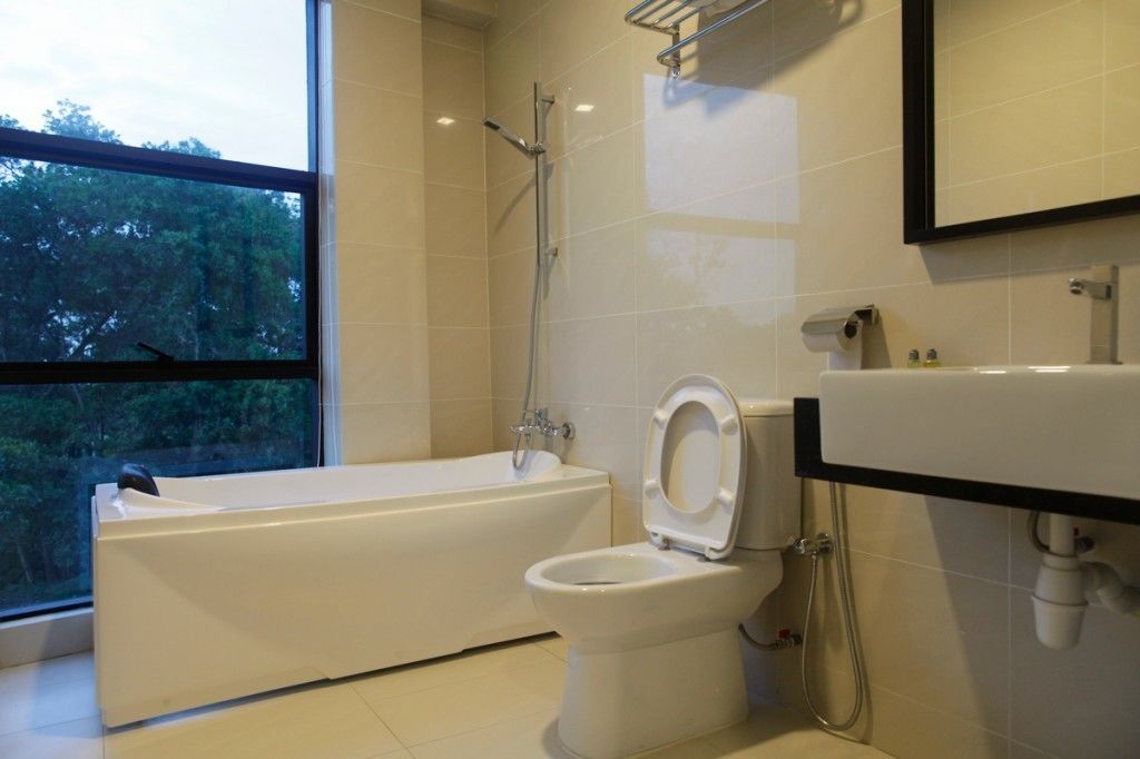 A modern bathroom with a bathtub, toilet, and a large window offering a view of trees.