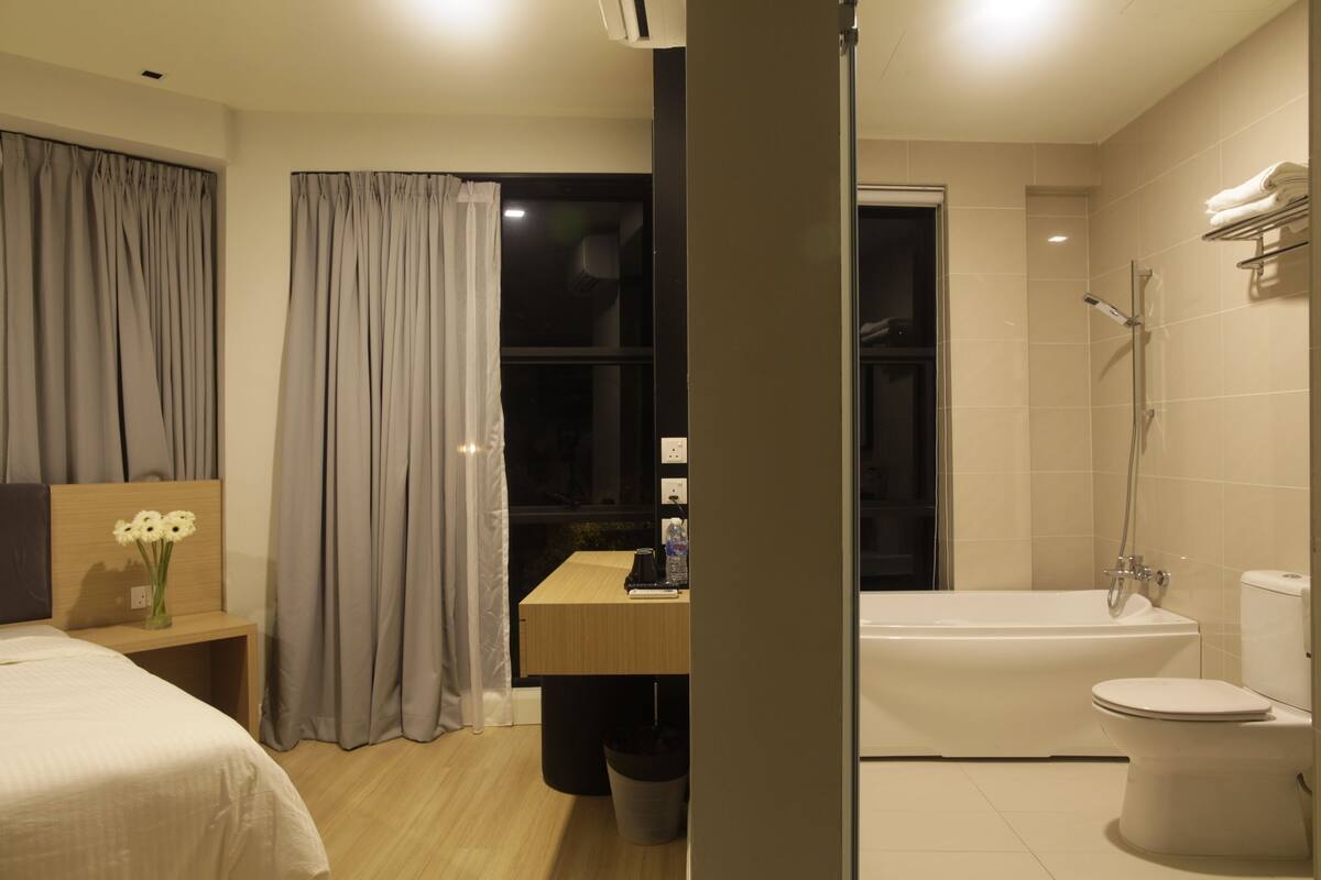 Una habitación de hotel moderna con una cama, una mesita de noche con flores, un escritorio, zona de ducha y un inodoro.