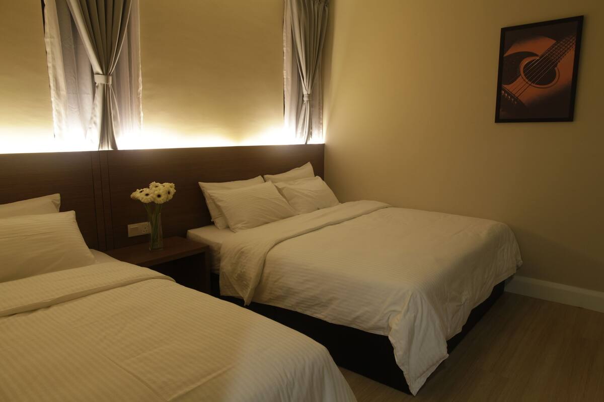 Habitación de hotel con dos camas, una mesita de noche con un jarrón de flores y un cuadro en la pared.