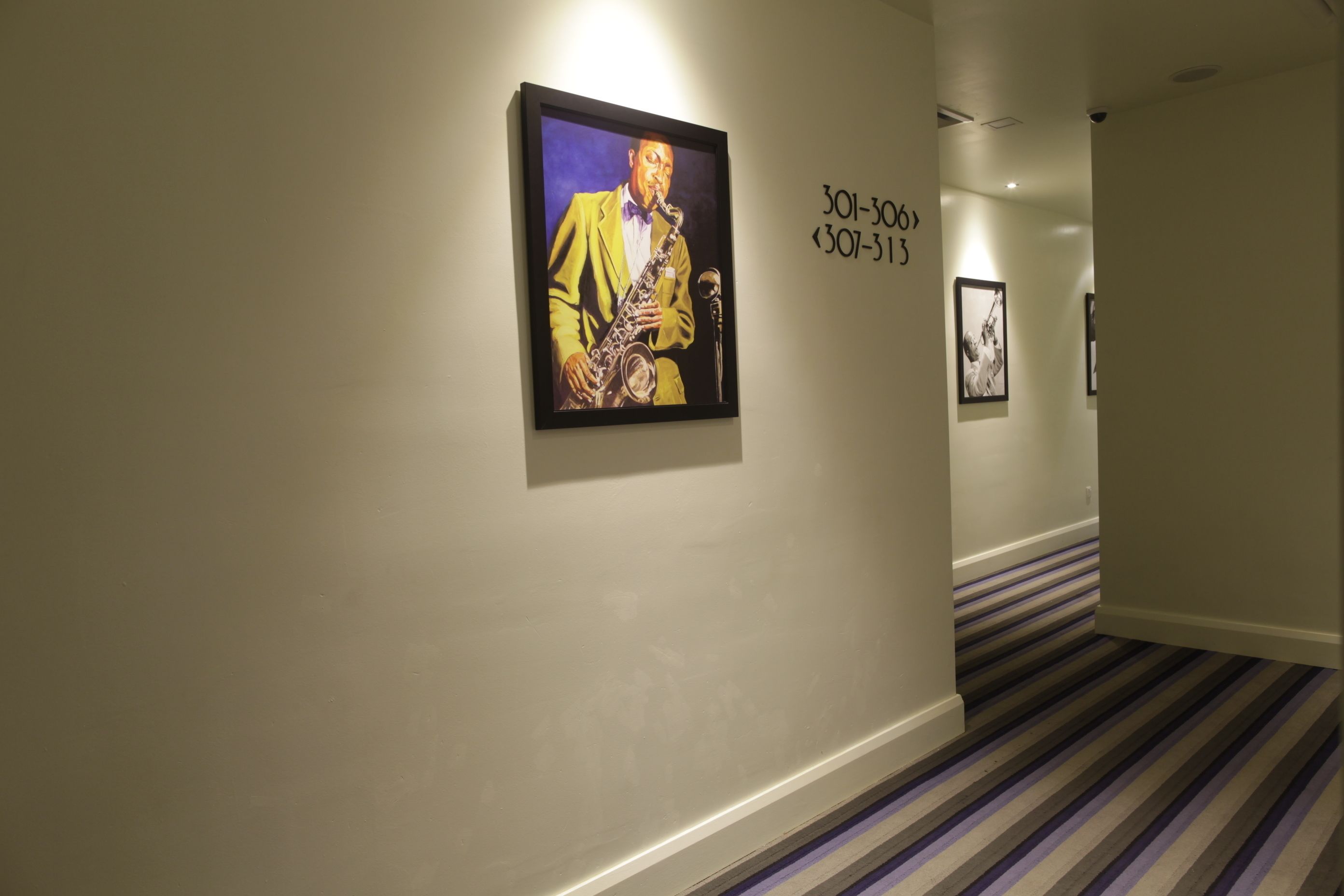 Een gang met een lijst met daarin een afbeelding van iemand die saxofoon speelt. Aan de rechterkant van de muur staan getallen.