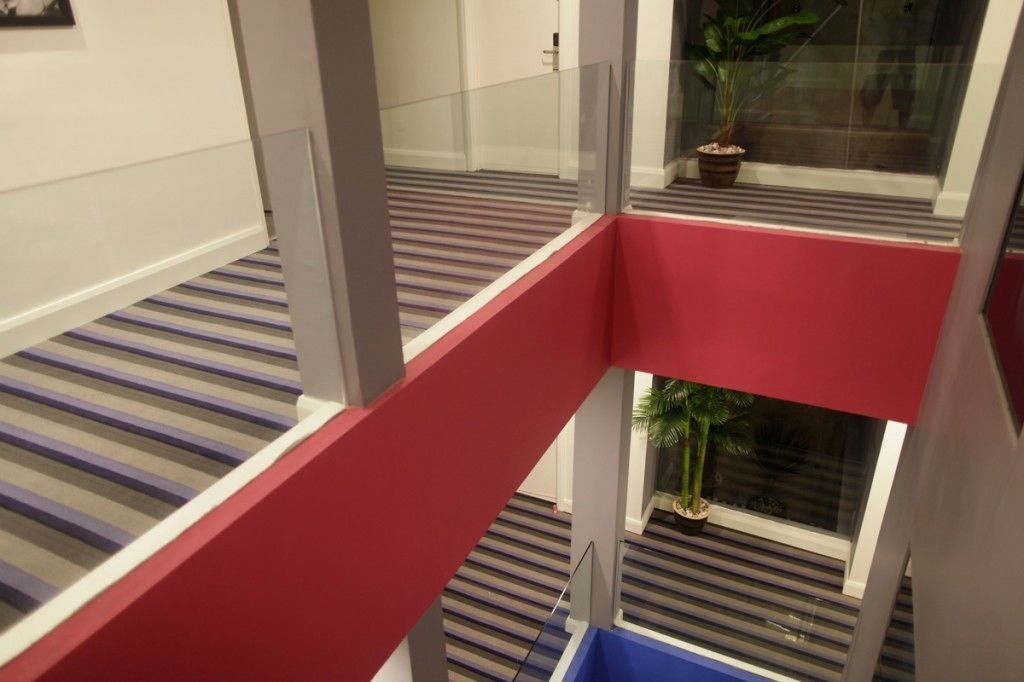A multi-level interior with a striped carpet, glass railings, and potted plants.