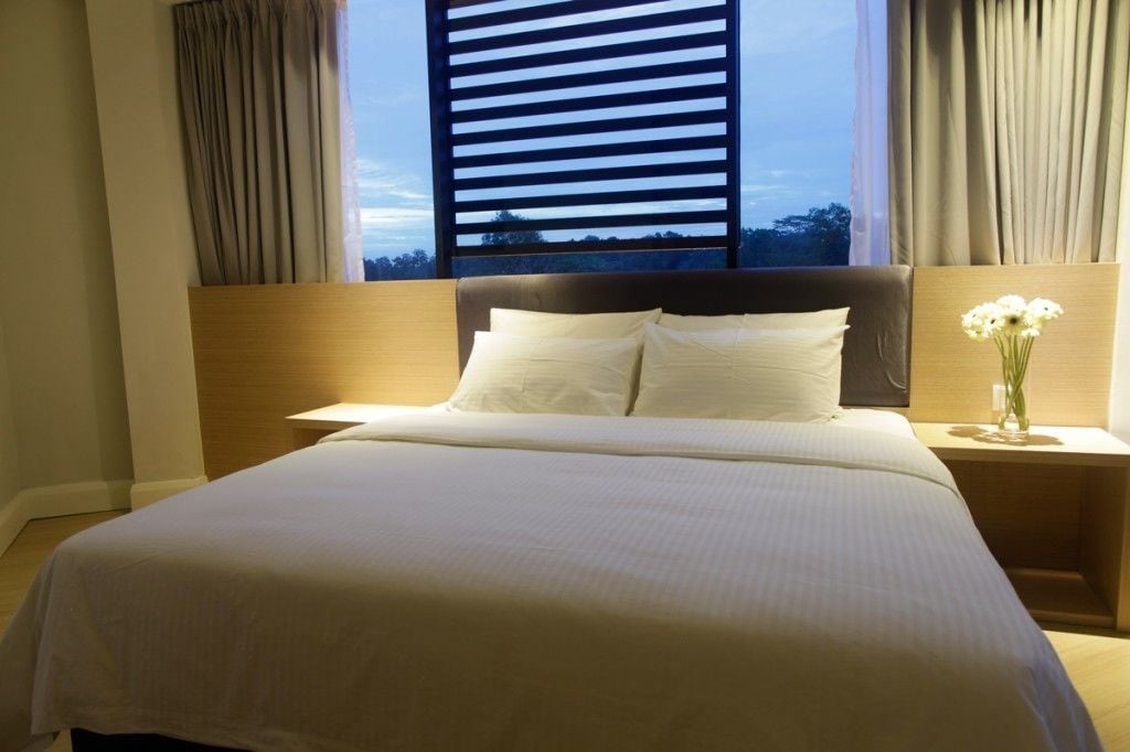 A hotel room with a large bed, a nightstand with a vase of flowers, and a window with curtains.