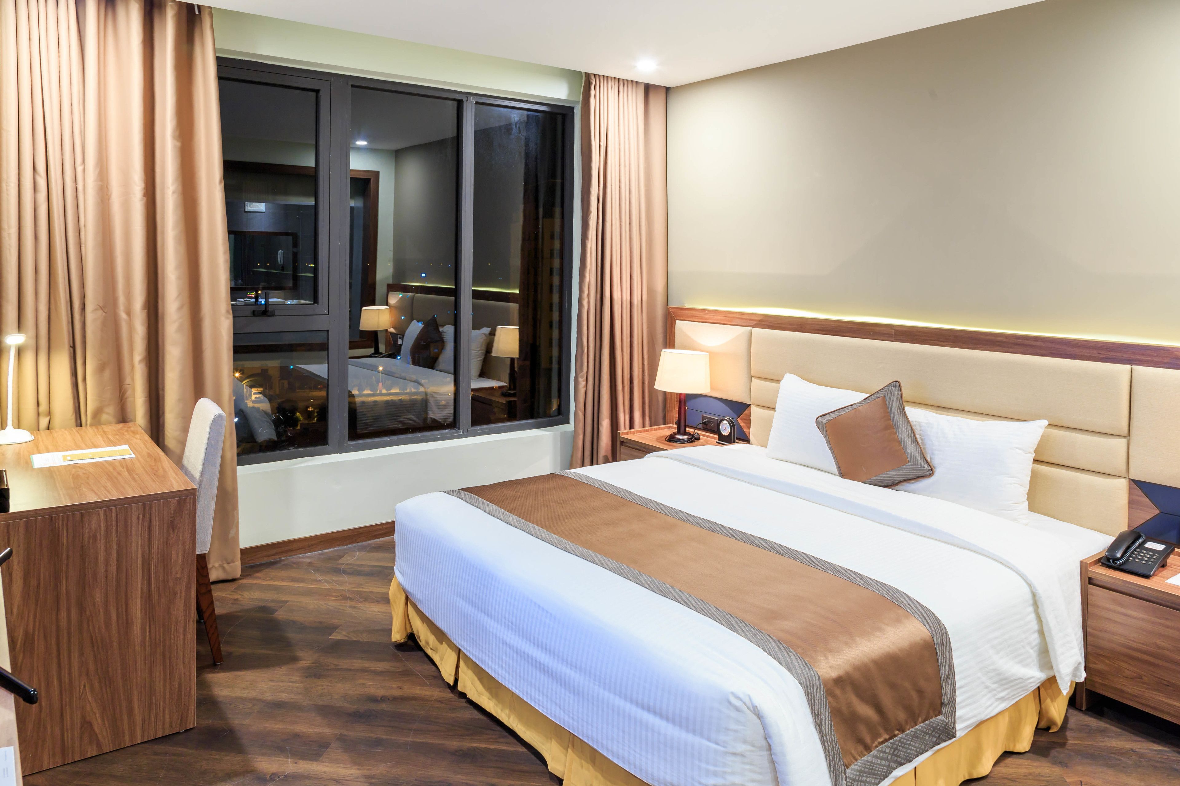 A hotel room with a large bed, a desk, and a window with curtains.