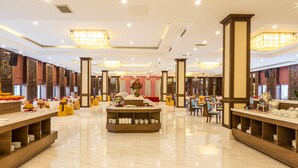 A spacious hotel lobby with a central reception desk, multiple seating areas, and a decorative floral arrangement.