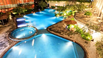 A large outdoor swimming pool with multiple sections, surrounded by lounge areas and greenery.
