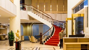 A spacious lobby with a grand staircase, a reception desk, and a decorative plant.
