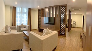 A modern living room with a flat-screen TV mounted on a wooden panel, two sofas, a coffee table, and a large window with curtains.