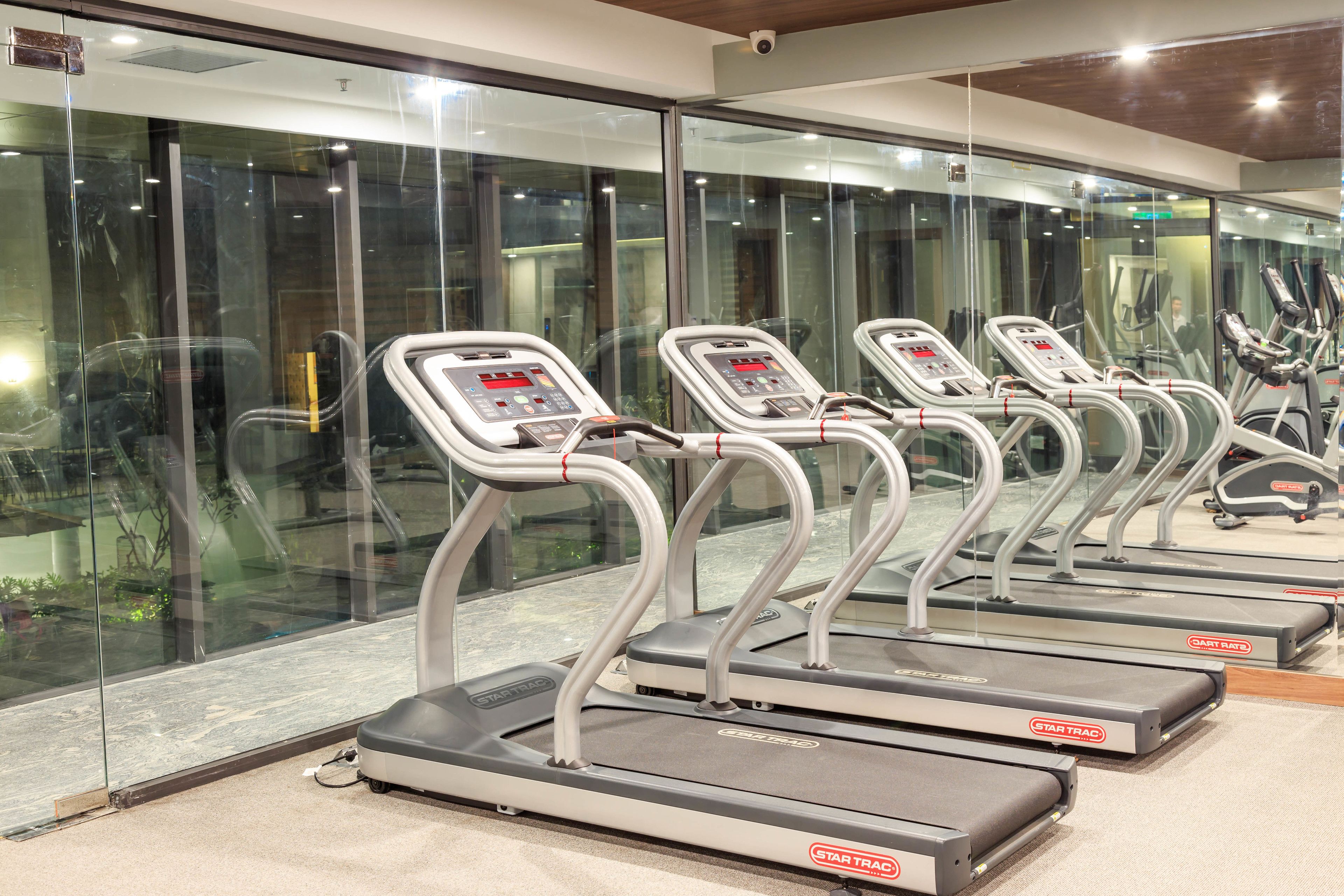 A row of treadmills in a gym with glass walls and a view of the outside.