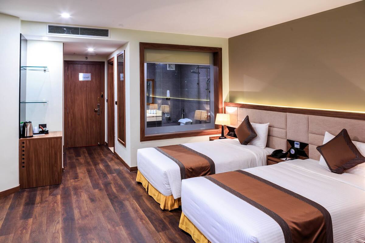 A hotel room with two beds, a small desk, a mirror, and a shower area.