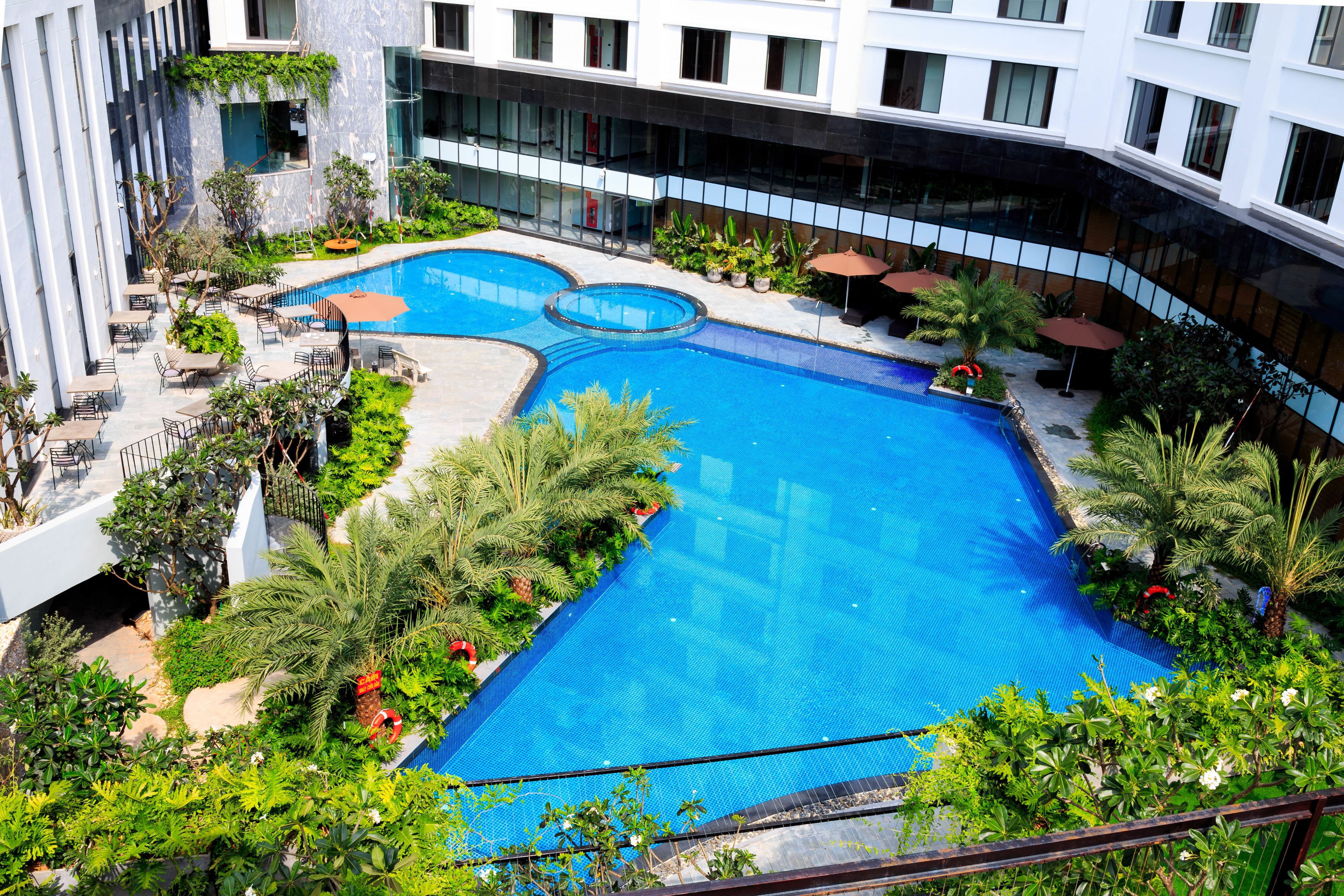 A rooftop swimming pool with multiple sections, surrounded by lush greenery and outdoor seating areas.