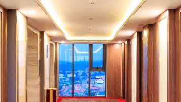 A hotel corridor with a red carpet, wooden paneling, and a view of a cityscape through large windows.