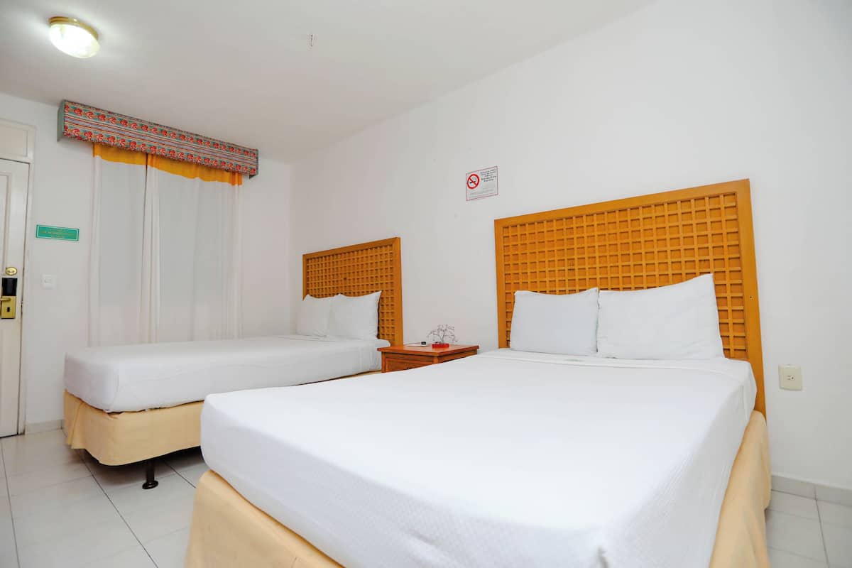 Una camera d'albergo con due letti singoli, una testiera in legno, un tavolino e una finestra con tende.