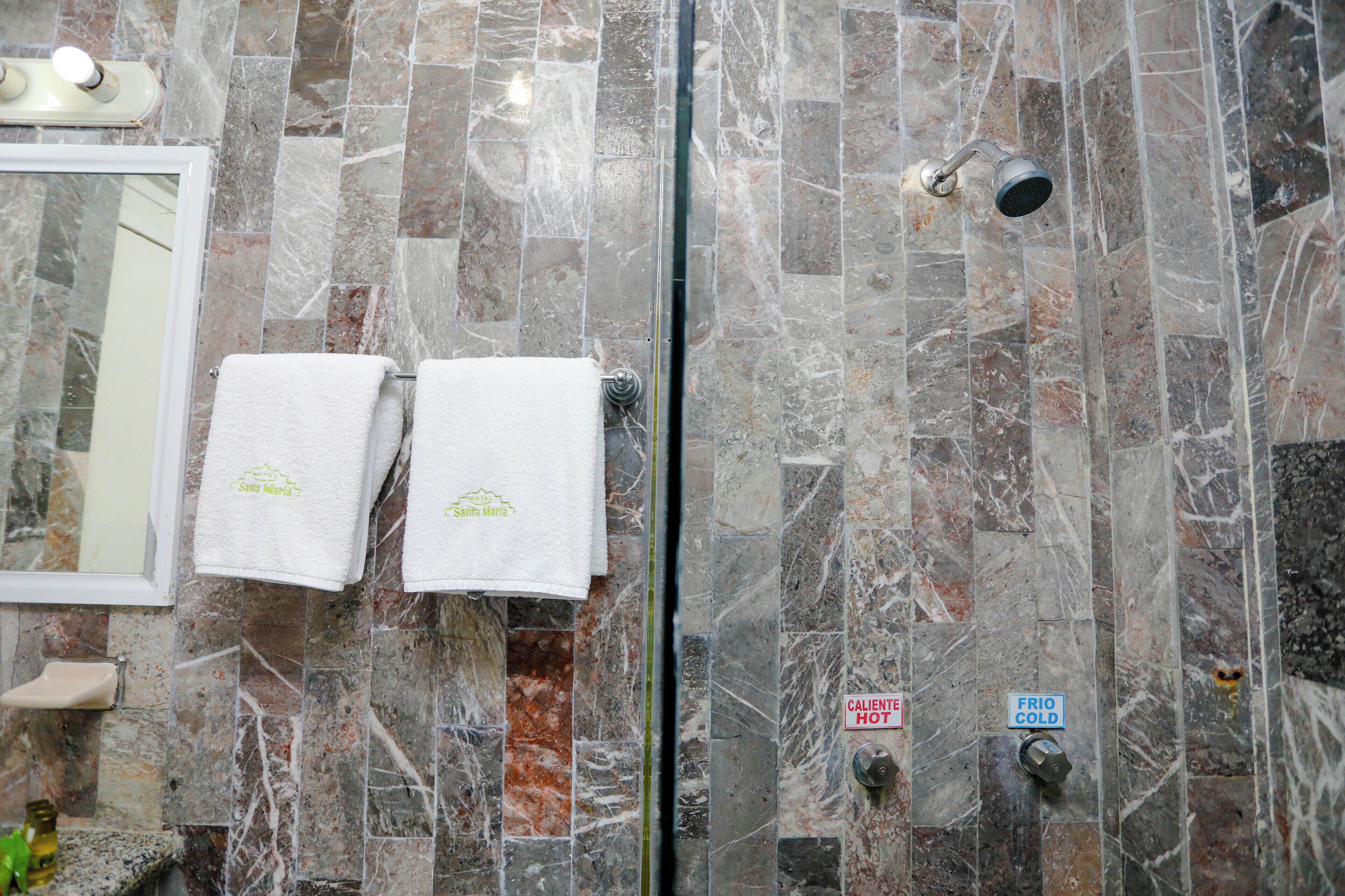 A bathroom with two white towels hanging on a rack, a showerhead, and a marble wall with a mix of gray and brown tiles.