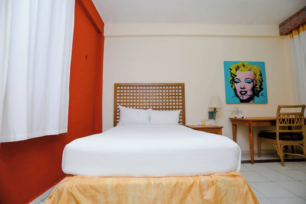 Una camera d'albergo con un letto, una scrivania, una sedia e un quadro appeso al muro.