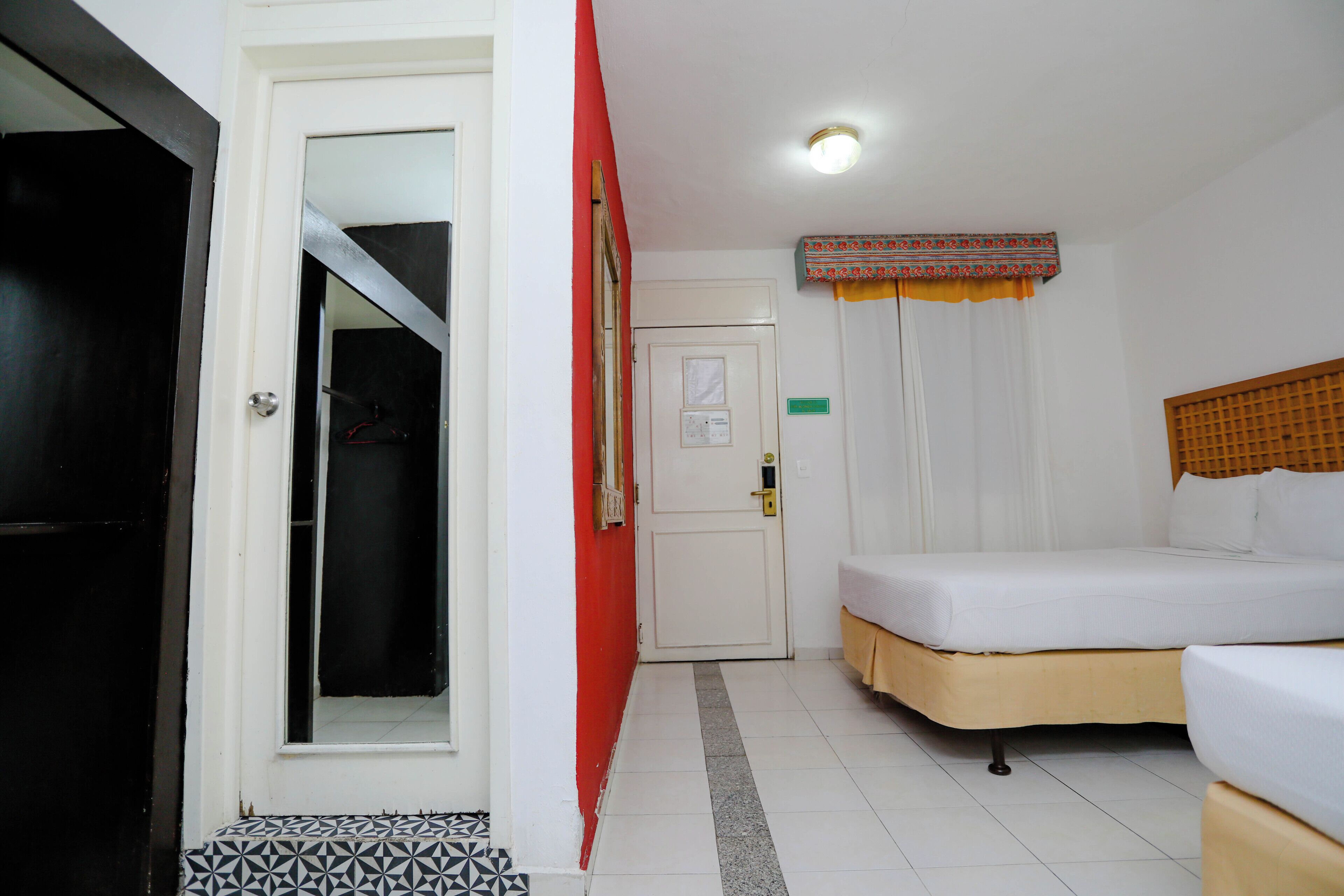 A hotel room with a bed, a wardrobe, a door, and a small window with curtains.