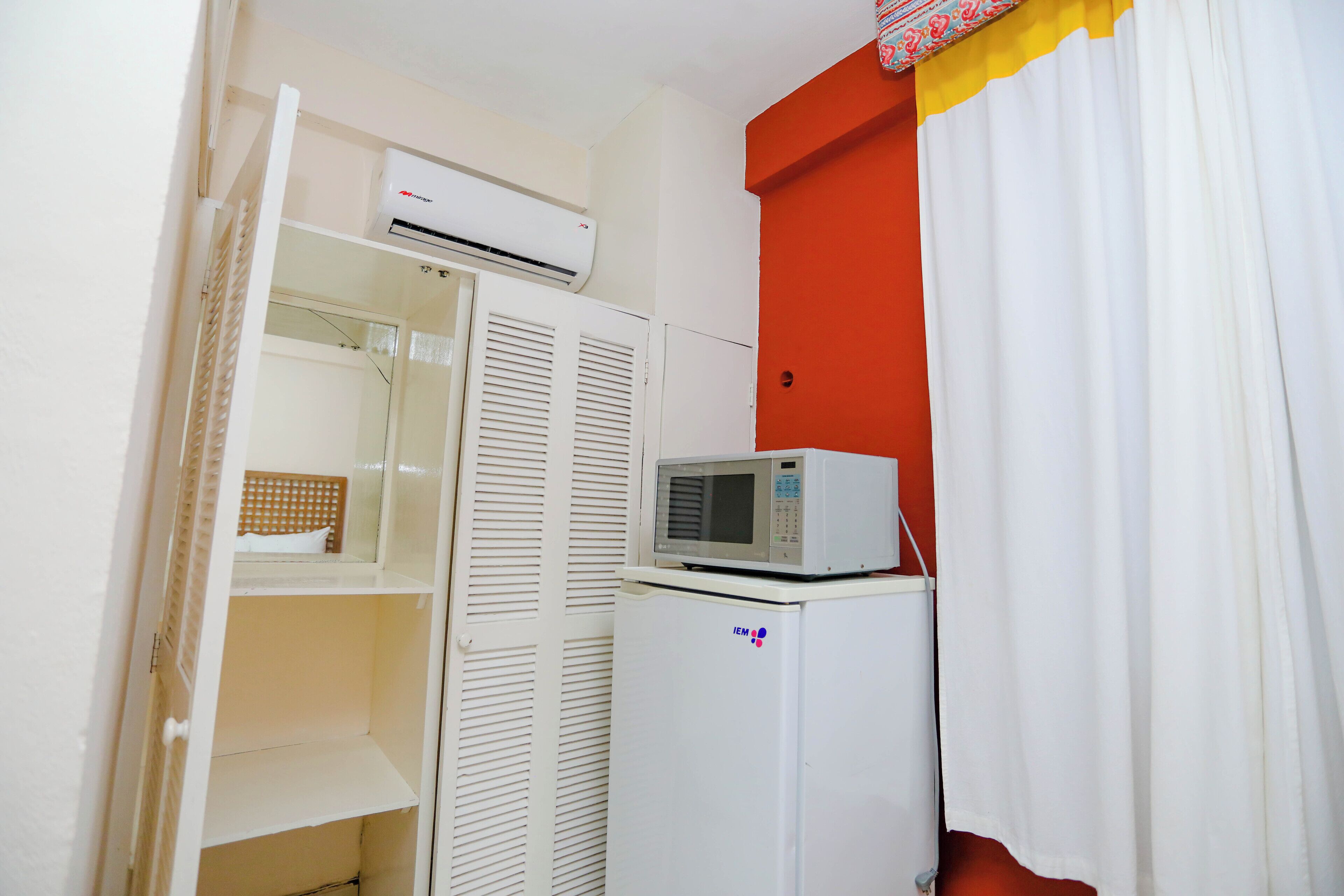 A compact room with a white wardrobe, a white refrigerator, and an air conditioning unit mounted above the wardrobe.