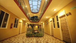 Un vestíbulo de hotel con una escalera central, techo de cristal y un extintor en la pared.